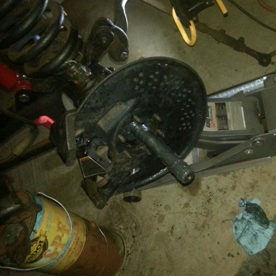 Close-up of vehicle suspension and brake assembly with coil spring, rotor, and axle.