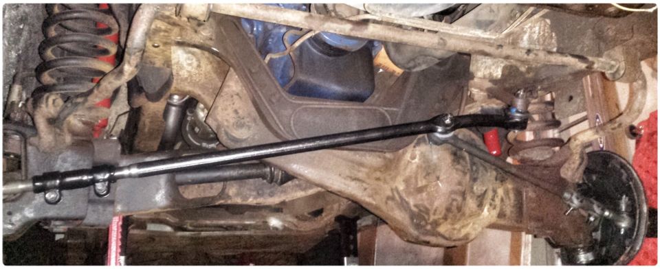 Underside view of vehicle suspension with new black tie rod assembly.