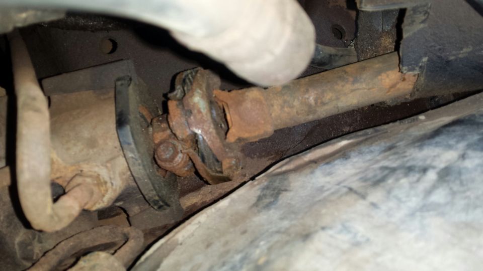 Heavily rusted driveshaft and universal joint assembly under a vehicle.