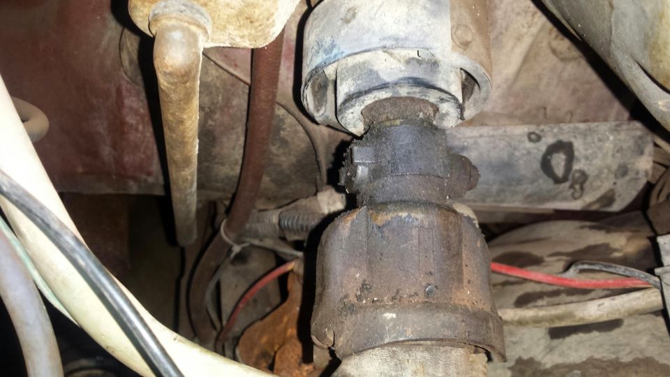 Close-up of a greasy, rusted steering column part with wires and metal components.