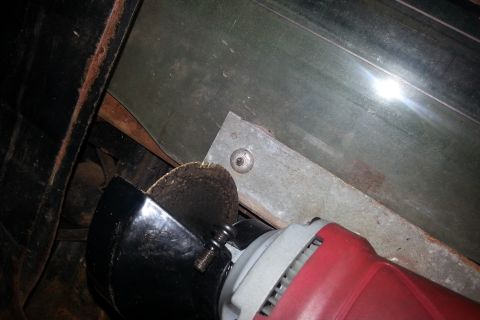 Angle grinder cutting metal bracket on vehicle undercarriage