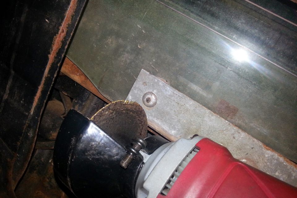 Angle grinder cutting a metal bracket on a green vehicle panel.