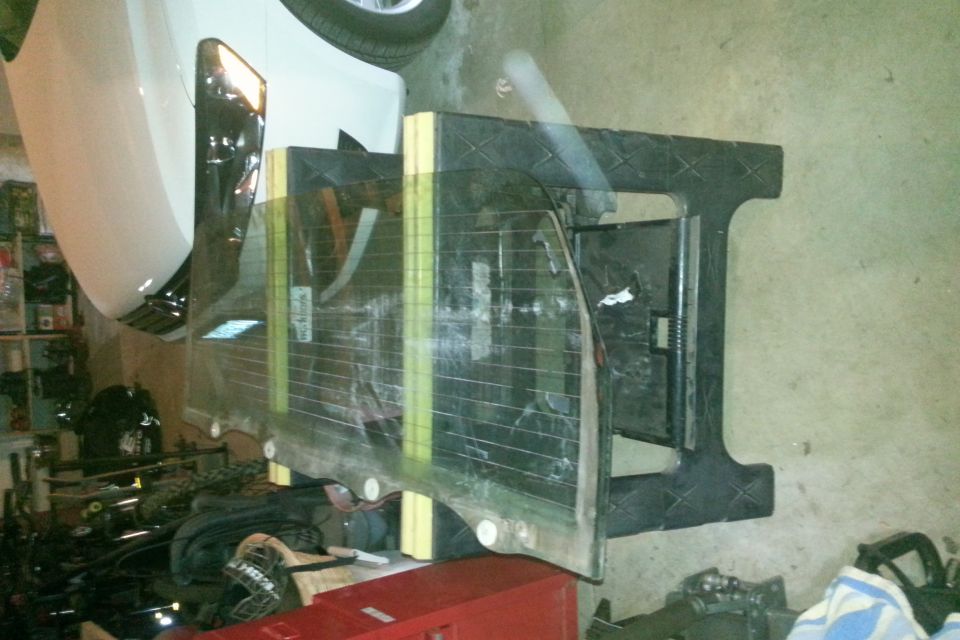 Rear window glass with defroster lines on a stand in a garage.