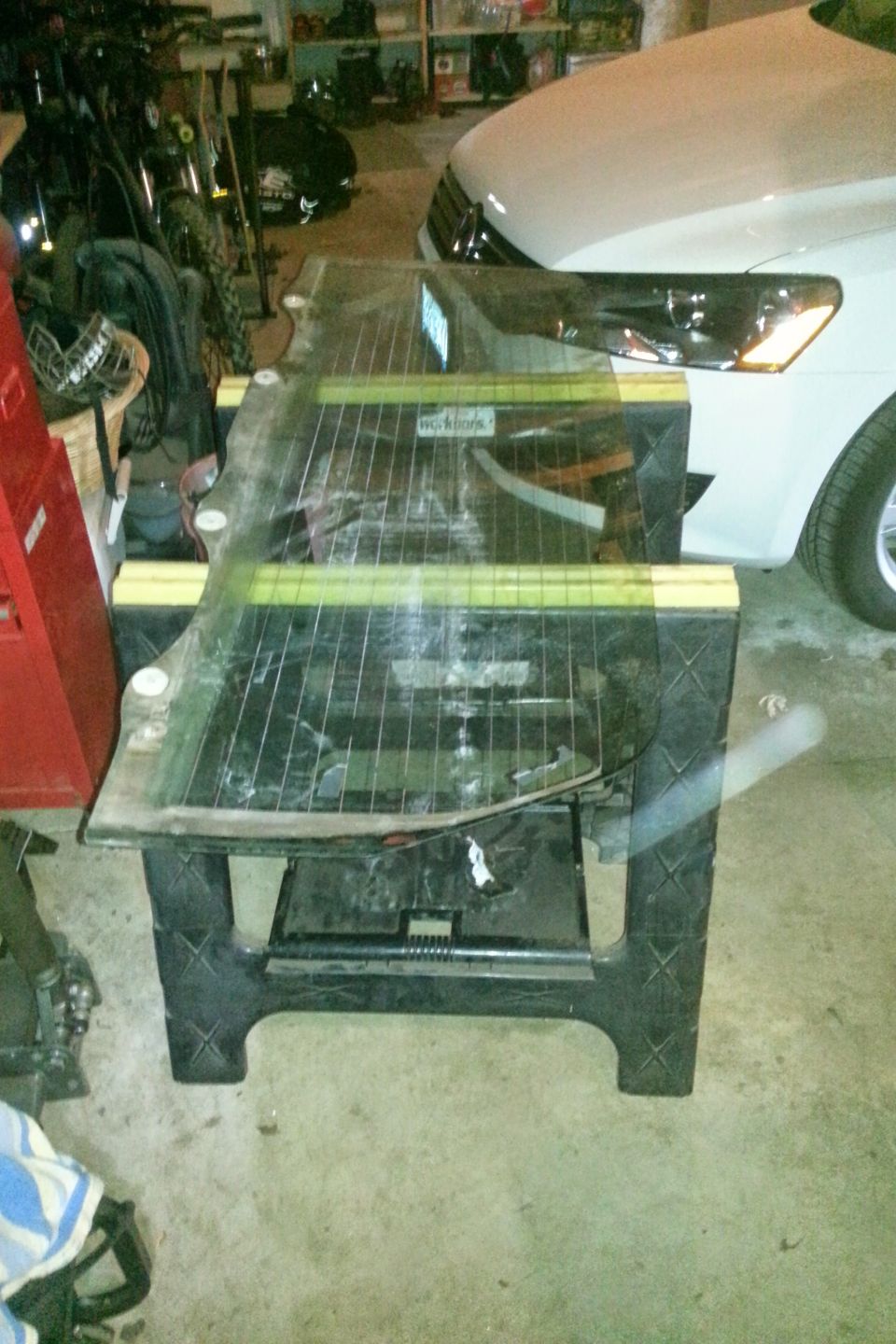 Large piece of glass on sawhorses in garage with white car in background.