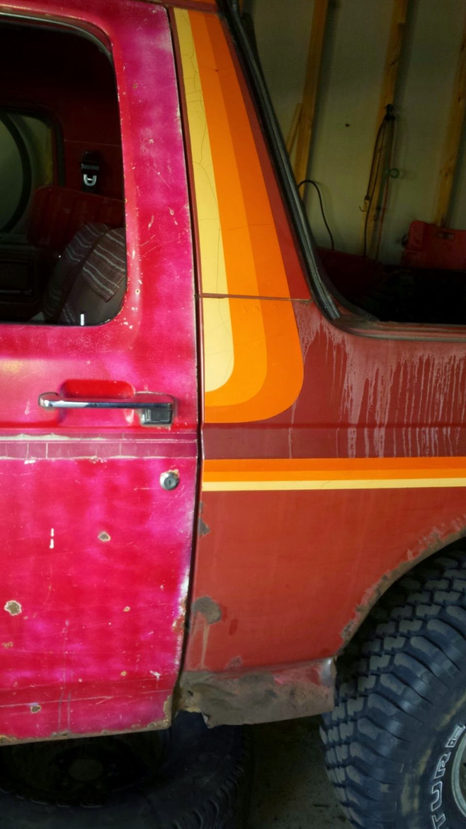Red 1984 Ford Bronco with retro stripe graphic, showing rust.