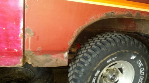 Close-up of rusted wheel well and tire on a red vehicle.