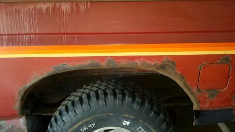 Close-up of rusted fender and fuel door on a red vehicle.