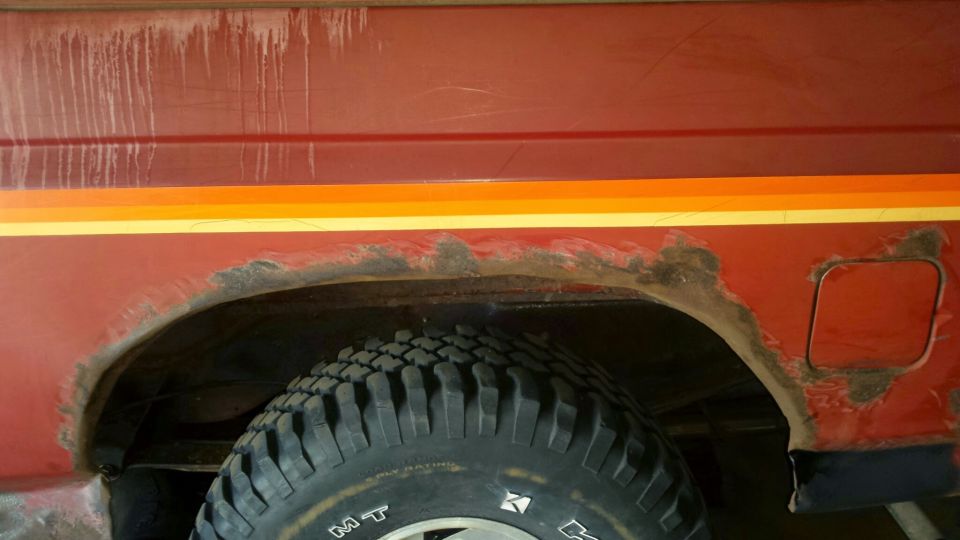 Close-up of rusted fender and fuel door on a red vehicle.