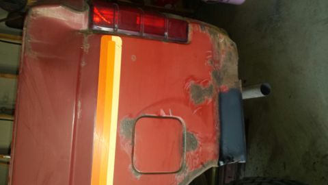 Red vehicle rear passenger side with stripes, fuel door, and taillight.