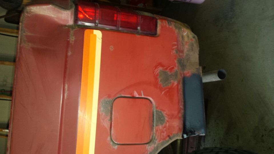 Red vehicle rear passenger side with stripes, fuel door, and taillight.
