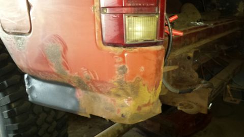 Close-up of a red vehicle's rear quarter panel with rust and a new patch near the tire.