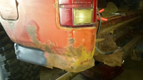 Rear passenger side of a red vehicle with rust damage and a new metal patch.