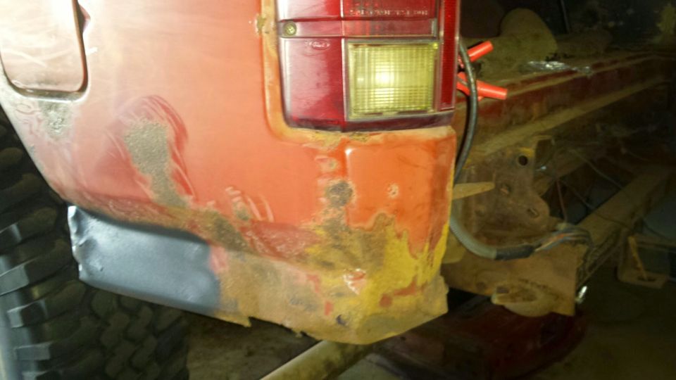 Rear passenger side of a red vehicle with rust damage and a new metal patch.