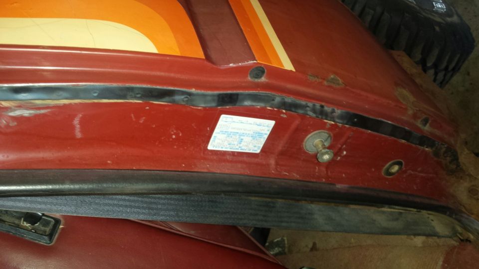 Interior door jamb of a red vehicle with a sticker and fasteners.