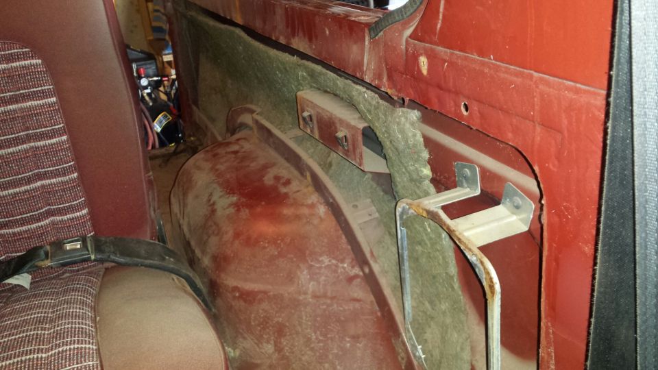 Interior of a red vehicle showing rear seat, metal panels, insulation, and a bracket.