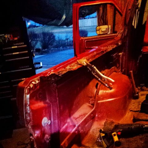 Red Ford Bronco interior with door removed, showing rust damage and tools.