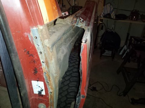 Rusted and riveted rocker panel and fender of a red vehicle.