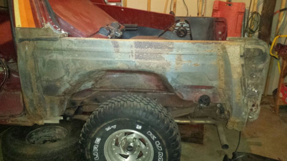 Rear view of a rusty vintage SUV with a spare tire in front.