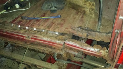 Rusted vehicle floor pan and rocker panel with a crowbar.