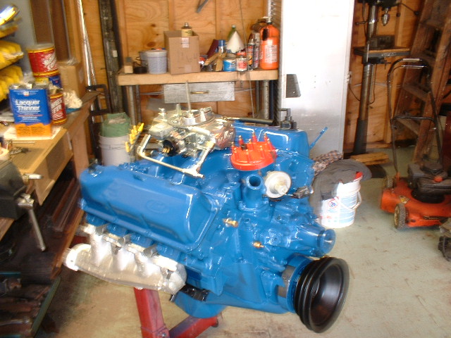 Blue V8 engine on a red stand in a garage. Carburetor and distributor cap are visible
