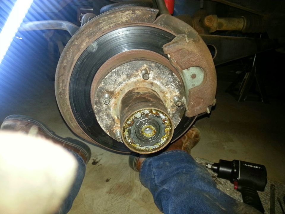 Rusty brake rotor and hub assembly with impact wrench and work boots.