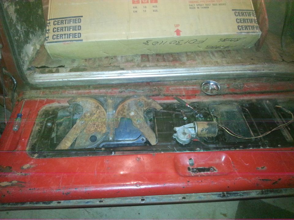 Open rear of a red vehicle showing a box and tailgate/window mechanism with motor and gears.