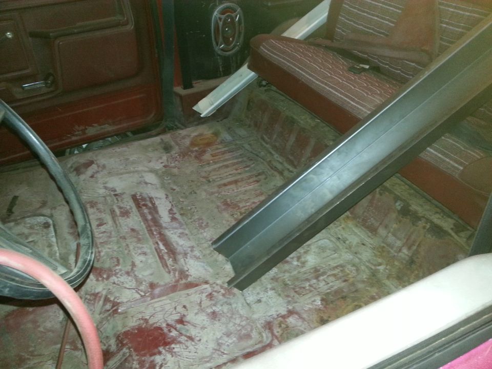 Interior of a classic Ford Bronco showing floorboards, reddish-brown seats, and a metal support beam.