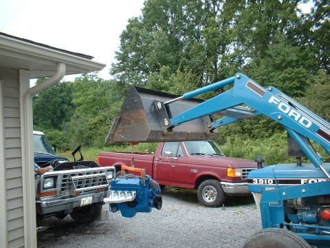 1978 Ford F-250 - A blue engine is being lowered by a Ford loader onto a red Ford pickup truck, with another Ford truck in the foreground.