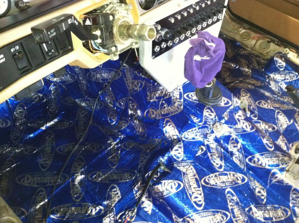 Car interior with sound deadening material on the floor and dashboard components exposed