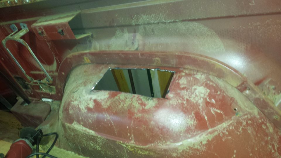 Red interior of a vehicle's wheel well with a cut-out opening. Metal bracing is visible