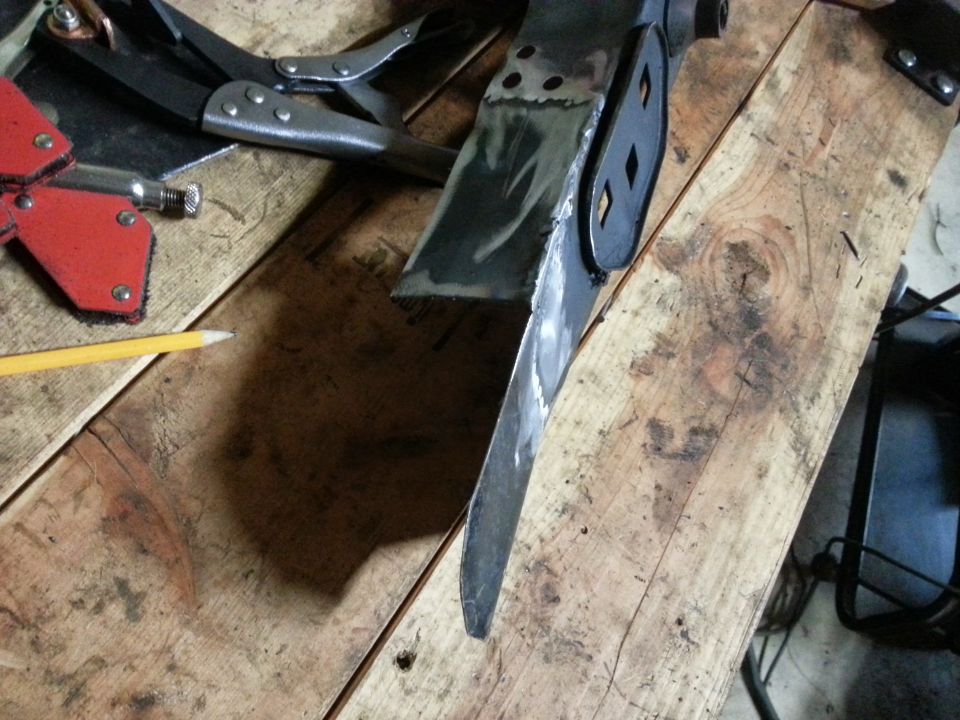 Welding clamp and pencil on a wooden workbench next to a metal part being worked on