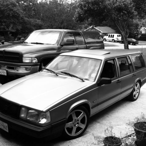 1991 Volvo 940 - A silver 1991 Volvo 940 wagon is parked in a driveway next to a pickup truck, with a white van and a dark sedan visible in the background.