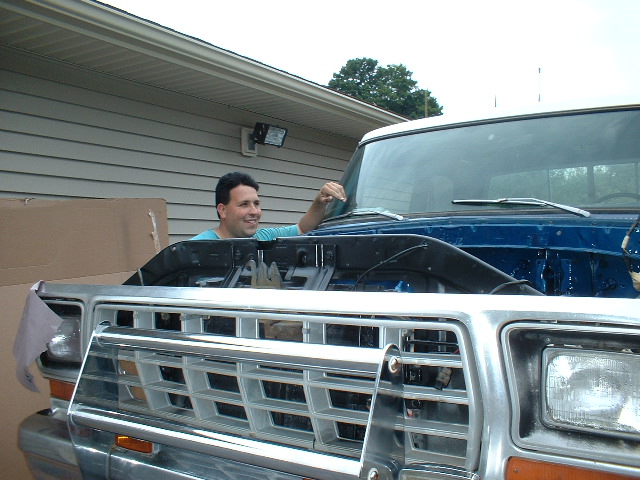 Man leaning over hood of blue pickup truck with chrome grille. Supermotors.net logo visible