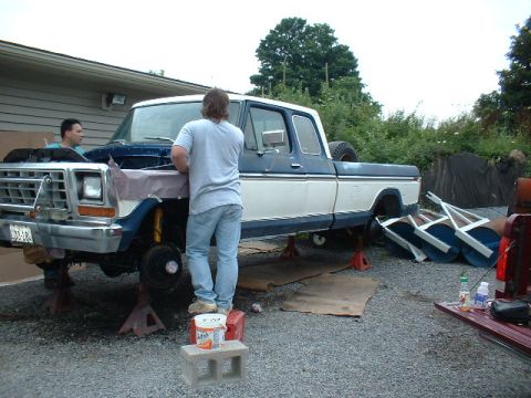 1978 Ford F-250 - Two men work on a 1978 Ford F-250 truck that is raised on jack stands with its hood open.