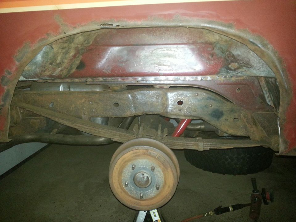 Underside of a red vehicle showing rust damage to the wheel well and frame.