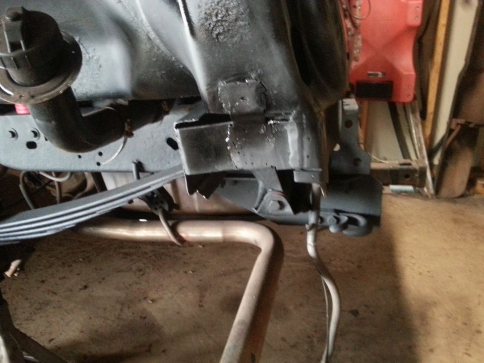 Underside of vehicle frame with leaf spring, exhaust pipe, and fuel tank assembly.