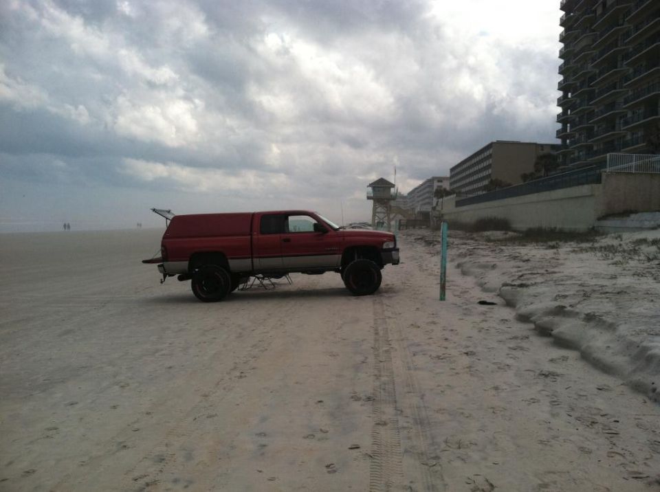 Red Dodge Ram pickup truck with camper shell on a beach.