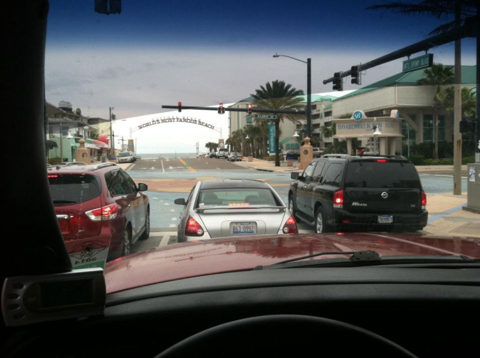 View from inside a car at a beach town intersection with traffic and a sign that says "WORLD'S MOST FAMOUS BEACH".