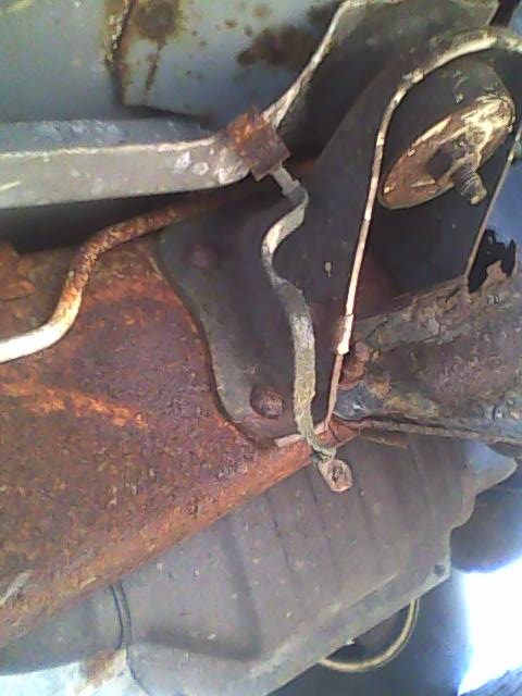 1994 Ford Bronco - Underbody photograph of a rusted bracket and linkage on the vehicle frame.