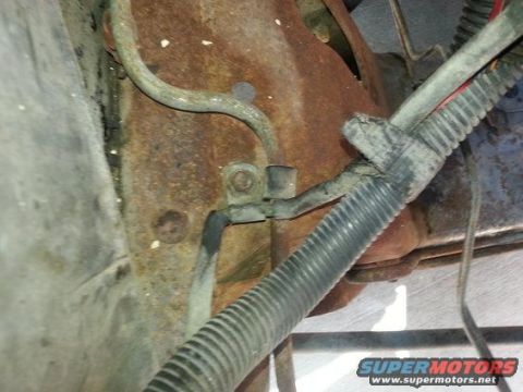 1994 Ford Bronco - Underbody photograph of a clamp securing wiring and tubing against a rusted panel.