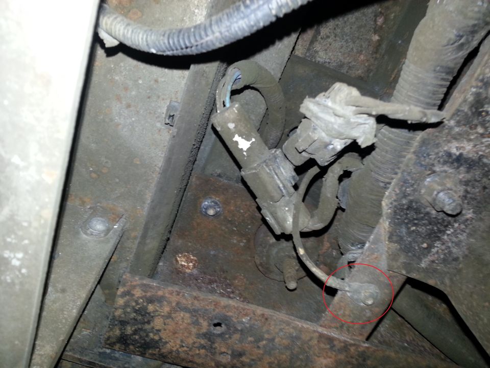 Underbody photo of brackets, wiring and a clamp with a fastener circled in red