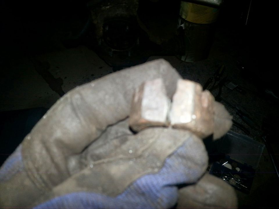 A gloved hand holding two rusty hexagonal nuts.