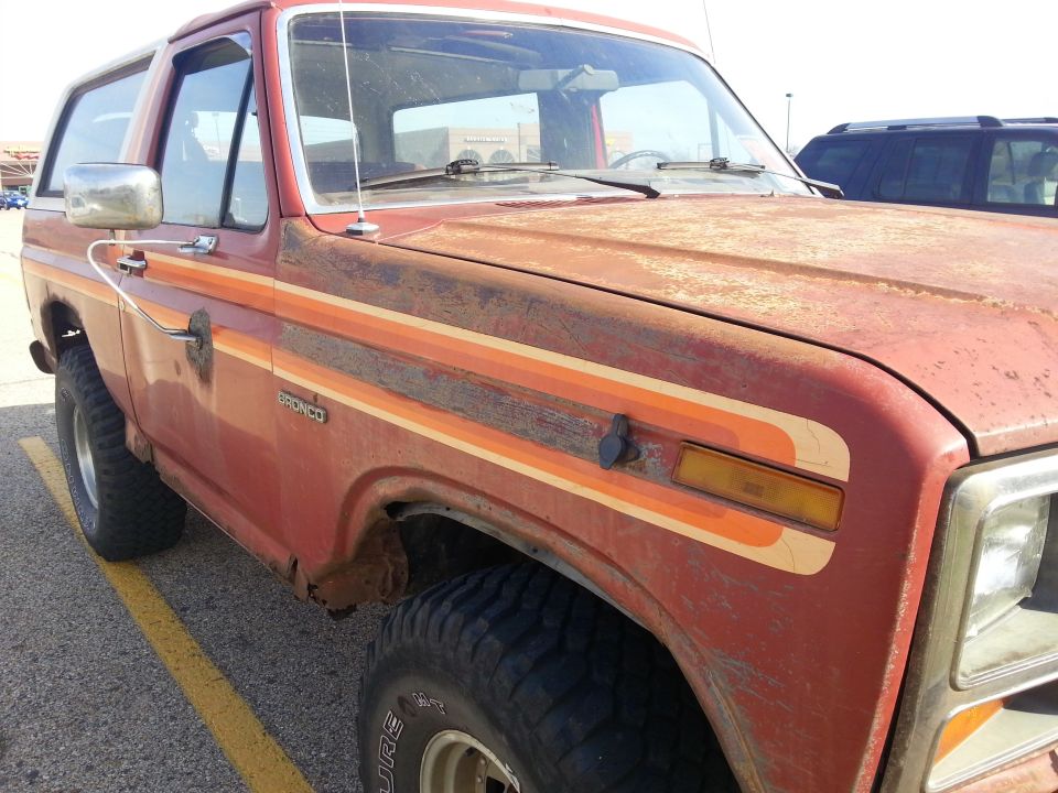 Weathered red 1984 Ford Bronco with rust and side stripes.
