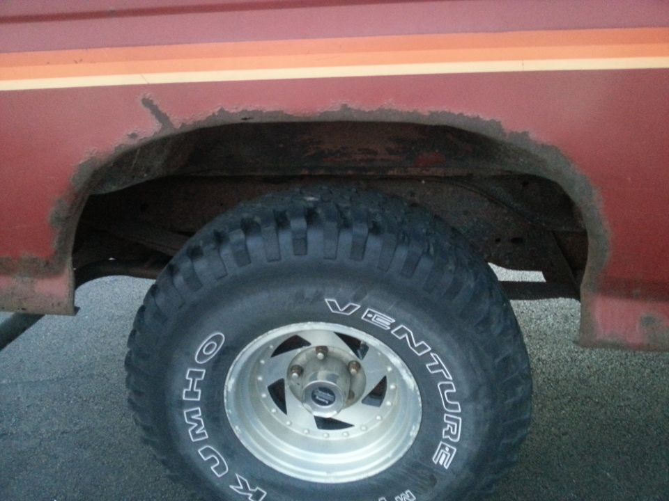 Red Ford Bronco rear wheel well with rust and off-road tire.