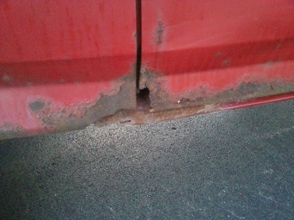 Close-up of rusted lower body panel on a red vehicle.
