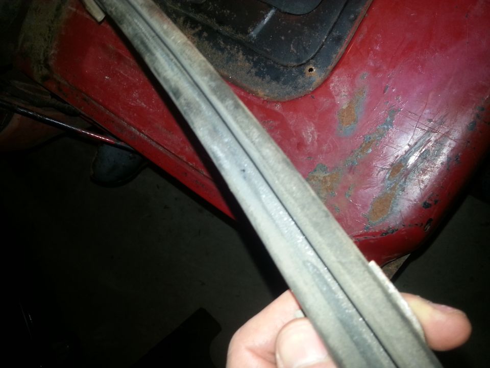 Close-up of a rubber seal being held against a red vehicle body with visible rust spots