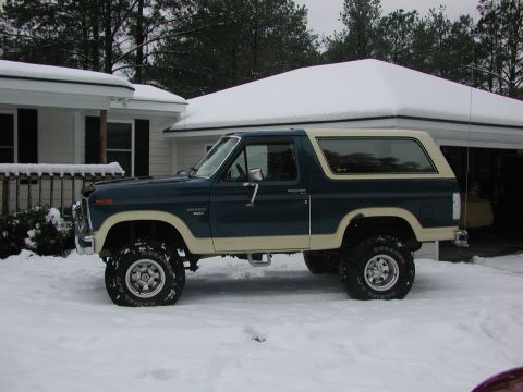 1985 Ford Bronco - A 1985 Ford Bronco with a two-tone paint scheme and lifted suspension sits in a snowy driveway.