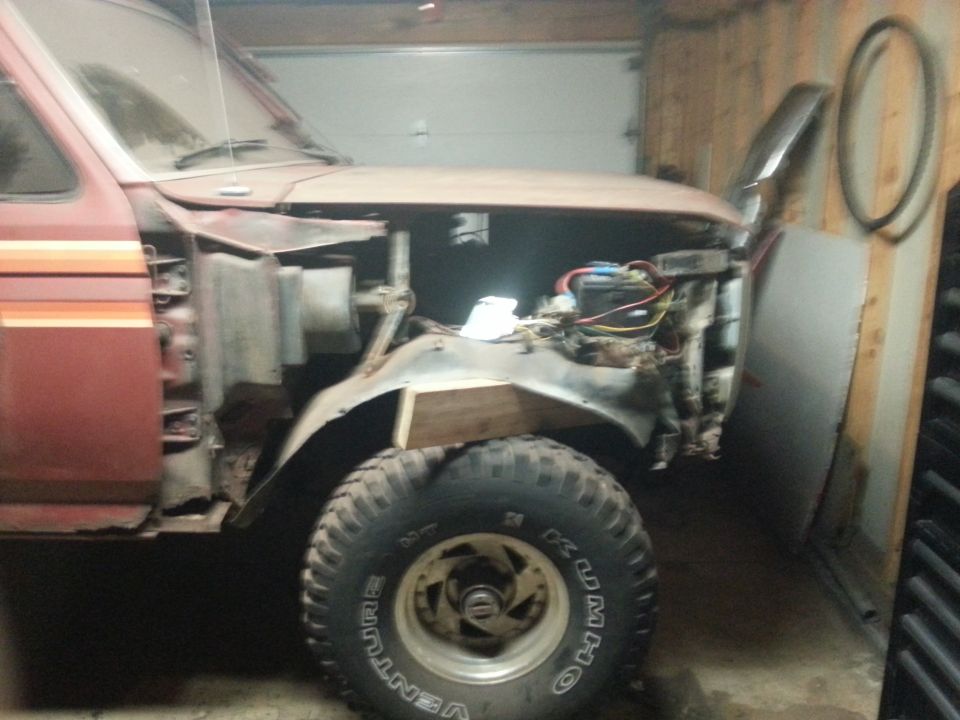 1980s red Ford Bronco with hood open, showing engine bay, in a garage.