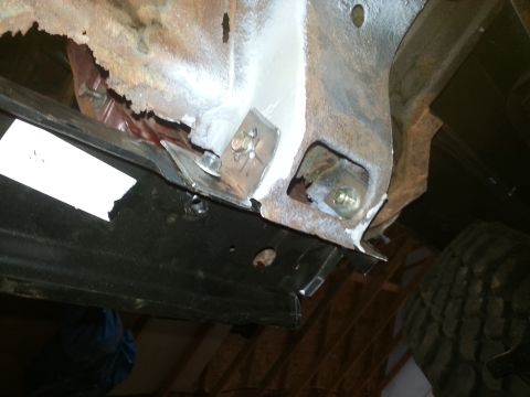 Close-up of rusty vehicle frame and black panel with bolts.