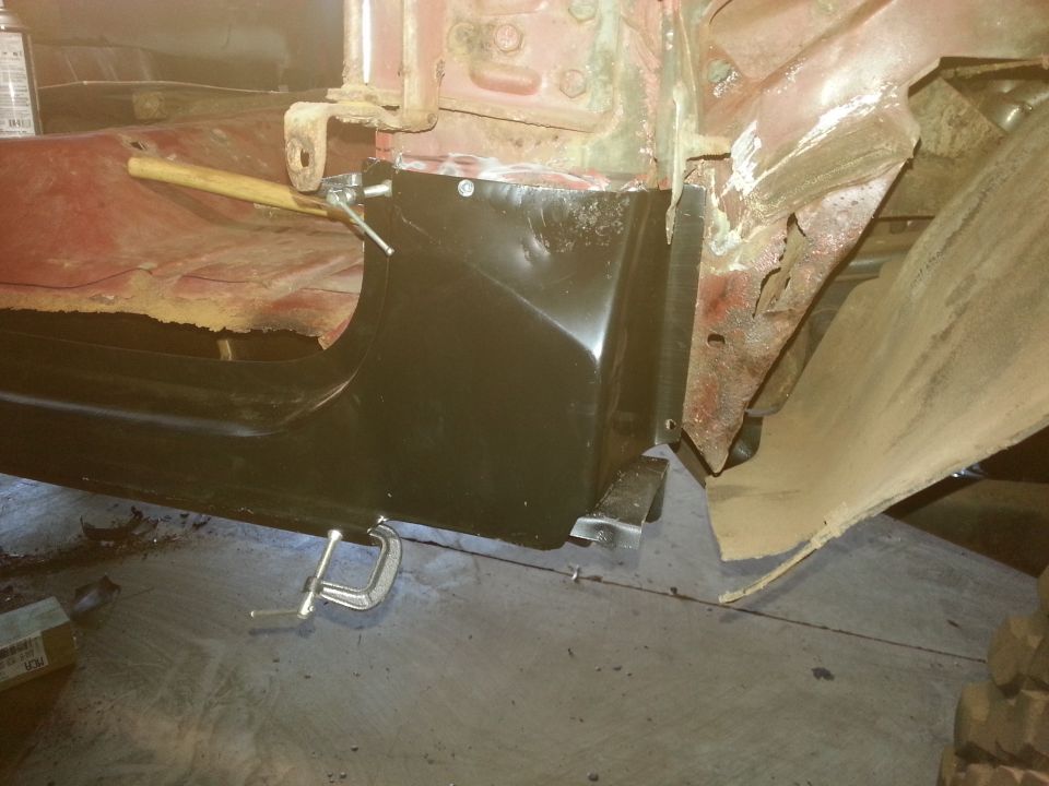 Black rocker panel patch clamped to a vehicle body with rusted metal visible.